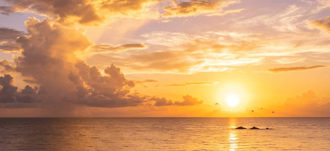 Couple walking along shoreline during vibrant sunset with golden sky and calm ocean